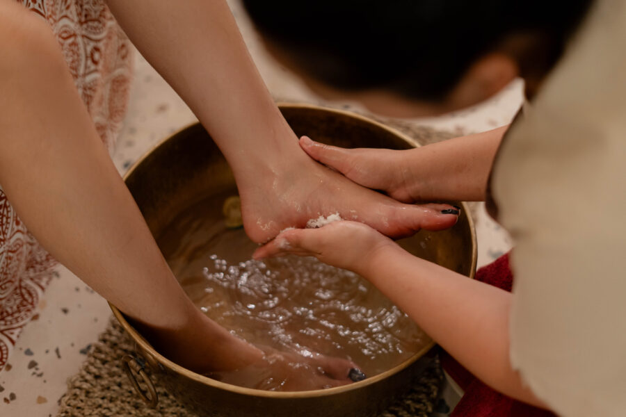 A therapist performing a traditional foot wash ritual with flower petals in a brass bowl as part of the October promotions at Jaens Spa Ubud, a premium spa bali destination.
