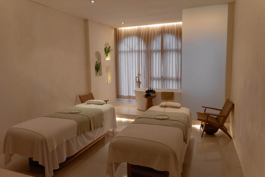 A calming, neutral-toned couple's treatment room featuring two massage beds and an elegant bathtub for ultimate relaxation at Jaens Spa Ubud.